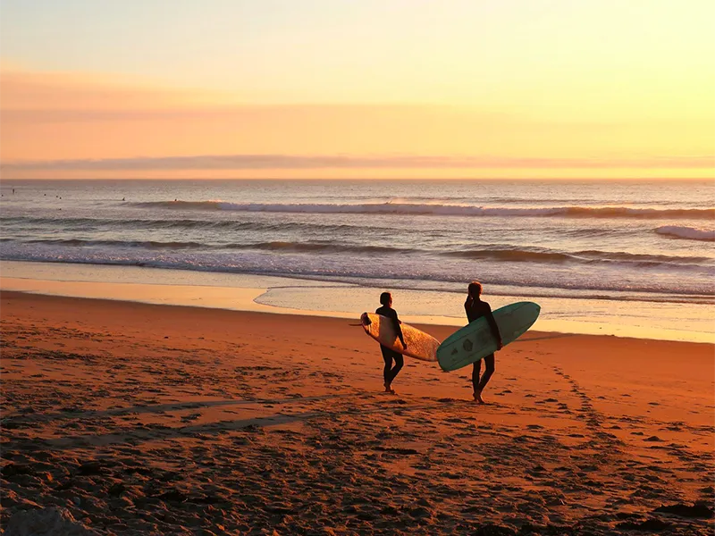 Deux surfeurs marchant sur la plage au coucher du soleil, planches sous le bras, Côte Landaise.